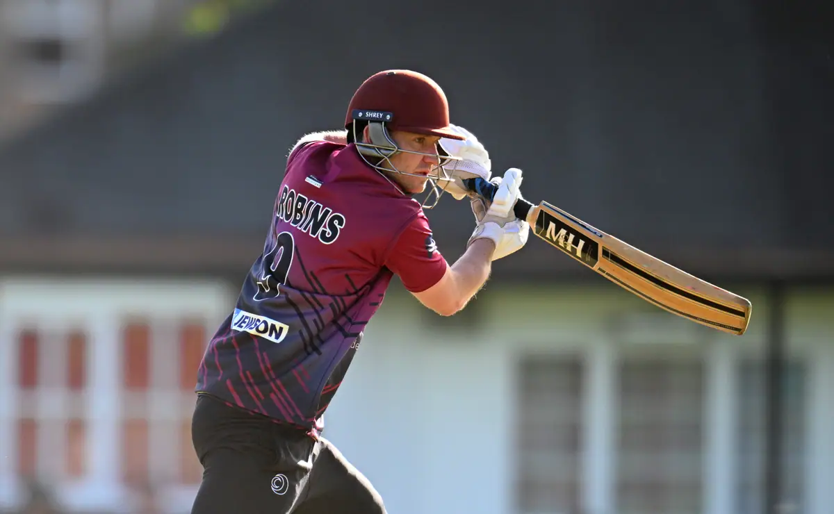 Close up of a Wadebridge batter in a claret helmet, bat angled across his body, pavilion windows behind.