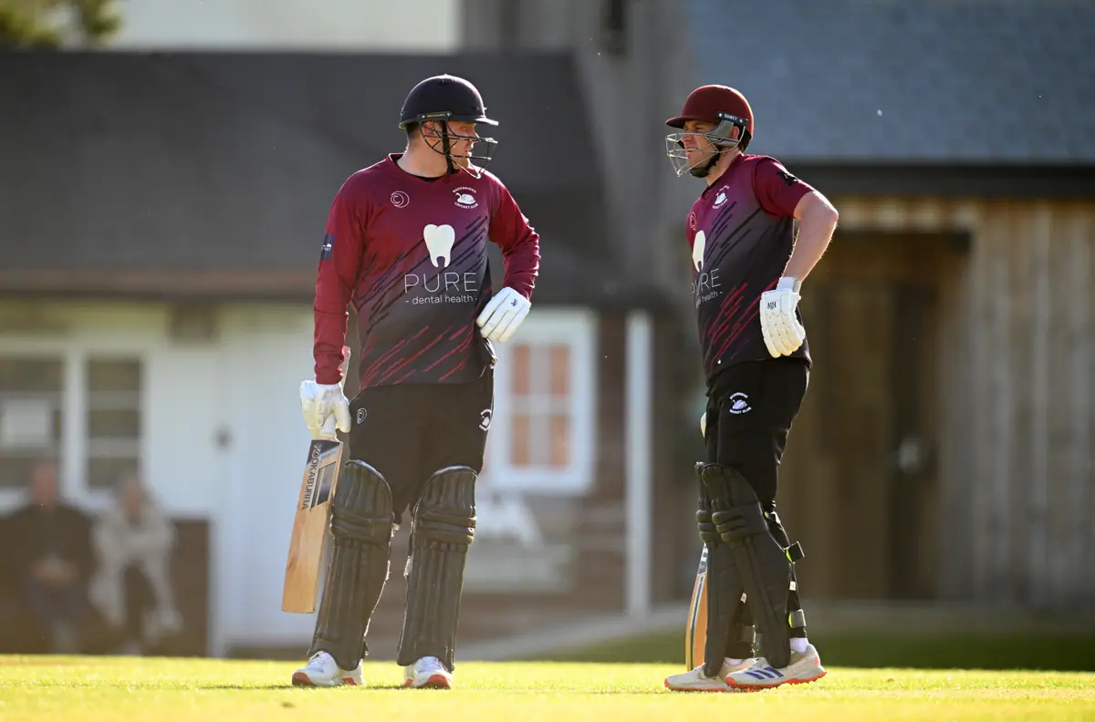 Two Wadebridge batters in conversation between overs, the white pavilion behind.