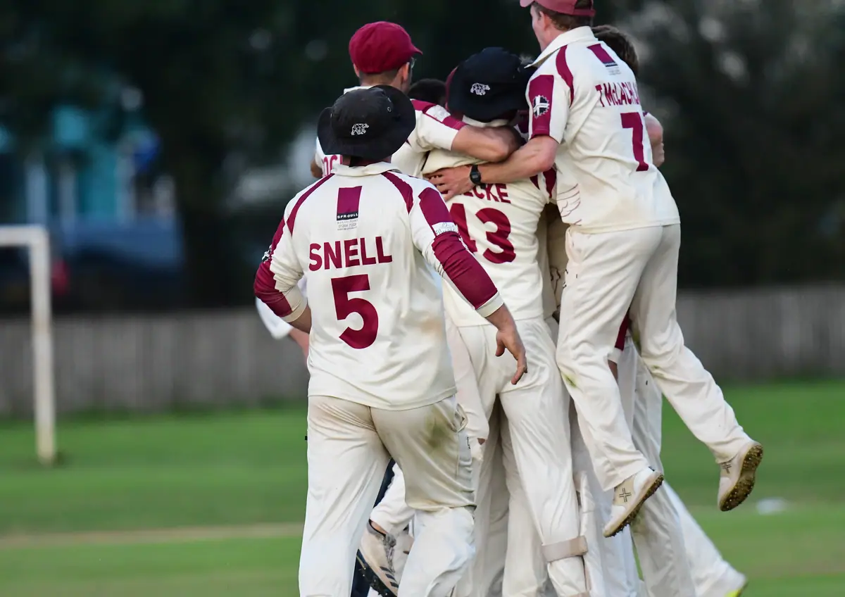 Wadebridge players in whites and claret caps leap on each other in celebration, Snell number 5 in the middle of the pile.